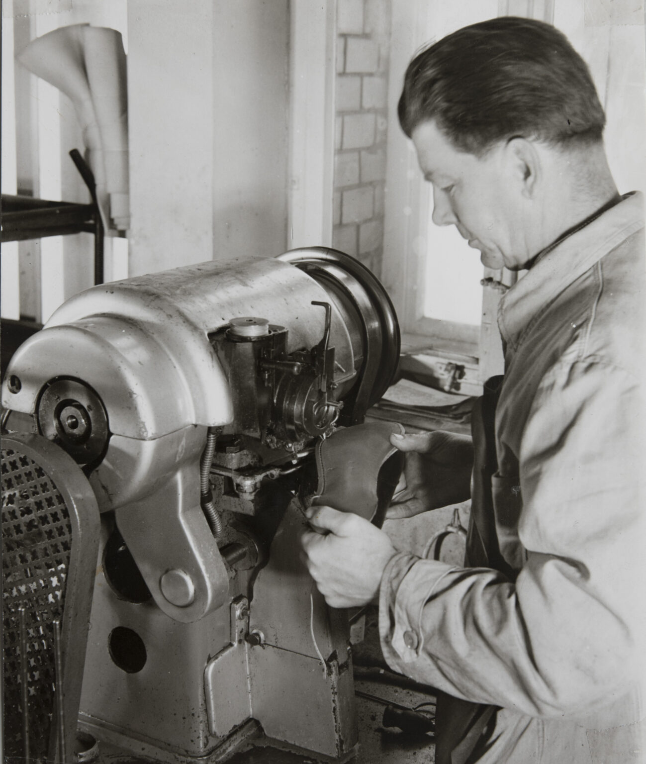Historisches Foto: Arbeiter bearbeitet Lederschaft an Maschine in der Schuhfertigung