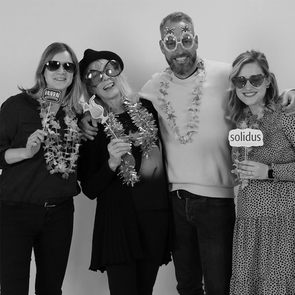 Vier Personen mit Party-Accessoires posieren vor Fotobox, Schwarzweiß