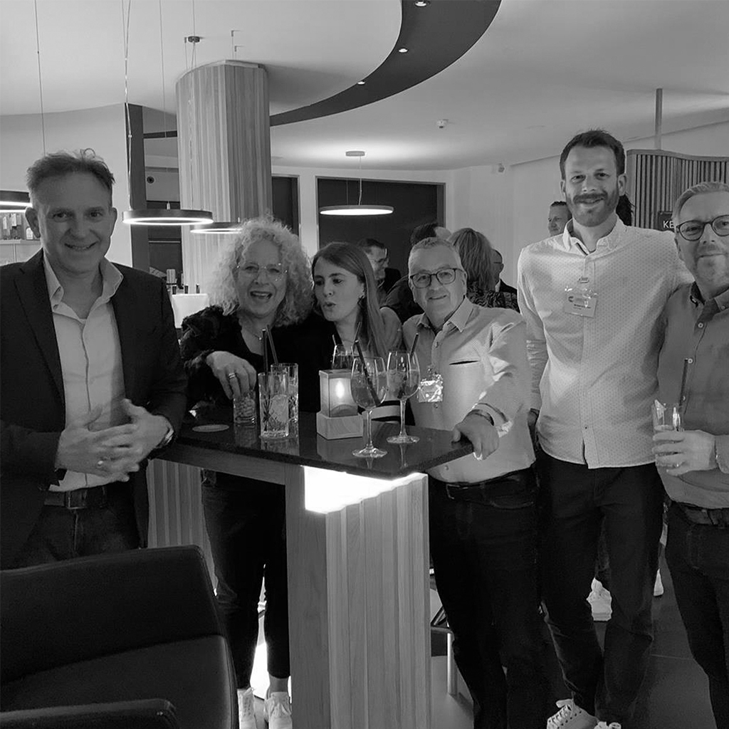 Gruppe von Kolleginnen und Kollegen steht lachend an einer Bar, Schwarzweiß