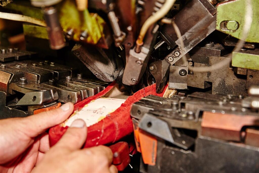 Solidus Produktion: Hand führt ein rotes Schaftteil in eine Maschine zur präzisen Verarbeitung – Schritt in der Schuhfertigung