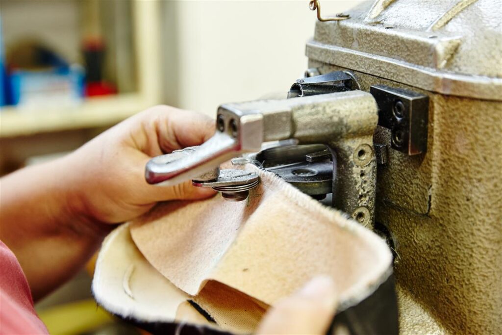 Solidus Produktion: Hand führt ein Lederteil an einer Maschine zur Kantenbearbeitung/Schärfung – Vorbereitung für die Schuhfertigung