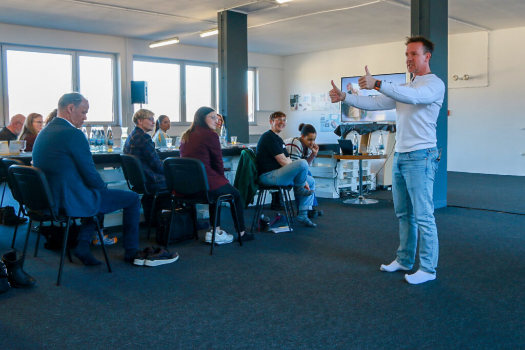 Trainer leitet eine Bewegungstherapie-Einheit bei der Solidus Academy, Teilnehmende sitzen im Seminarraum und schauen zu