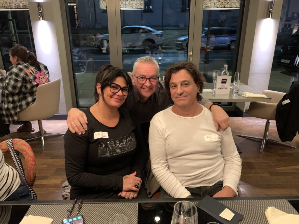 Drei Teilnehmende der Solidus Academy sitzen beim gemeinsamen Abendessen im Restaurant und lächeln in die Kamera