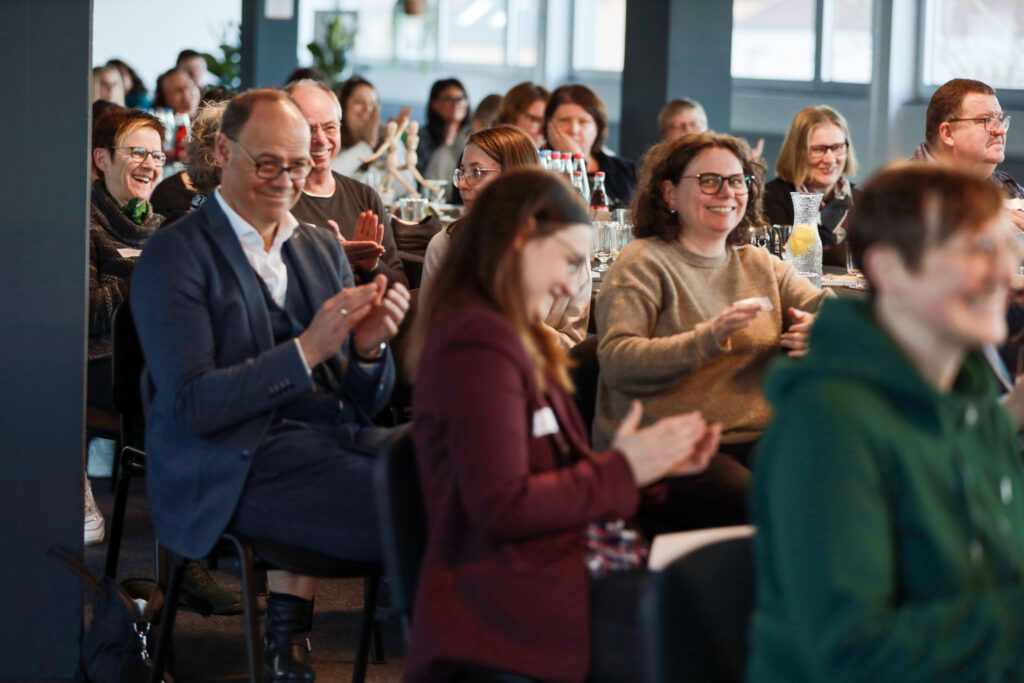 Publikum bei der Solidus Academy applaudiert im Seminarraum, Teilnehmende sitzen an Tischen mit Getränken und Notizen