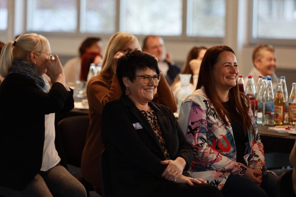 Teilnehmende der Solidus Academy sitzen im Seminarraum und lachen während eines Vortrags, auf den Tischen stehen Getränke