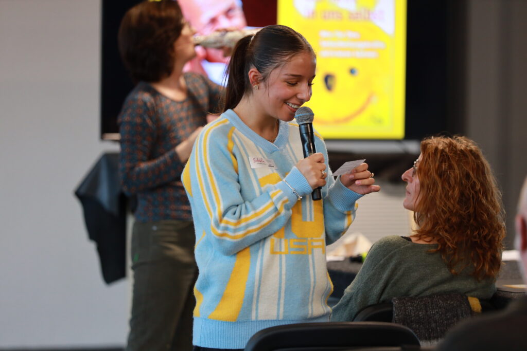 Interaktive Szene bei der Solidus Academy: Teilnehmerin spricht mit Mikrofon und Notizzettel mit einer Sitzenden im Seminarraum