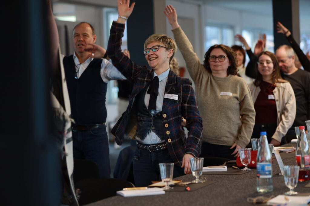 Teilnehmende der Solidus Academy stehen im Seminarraum und machen eine interaktive Übung mit erhobenen Händen