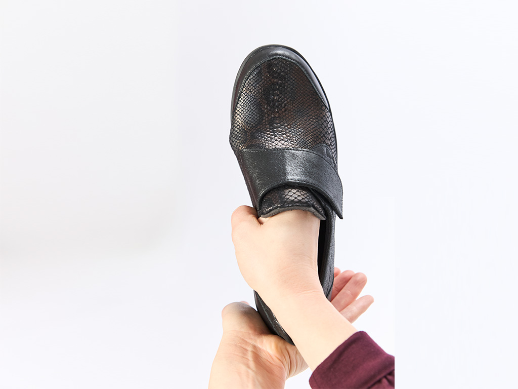 Hand hält einen schwarzen Solidus Damen-Klettschuh mit strukturierter Lederoptik – bequemer Einstieg und flexible Passform