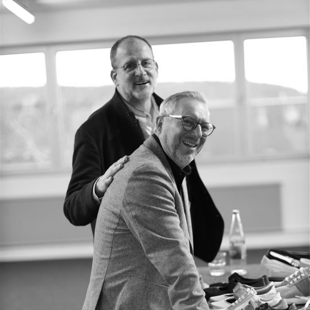 Zwei Solidus Kollegen im Gespräch, schwarzweißes Foto im Büro/Meetingraum mit freundlicher Geste