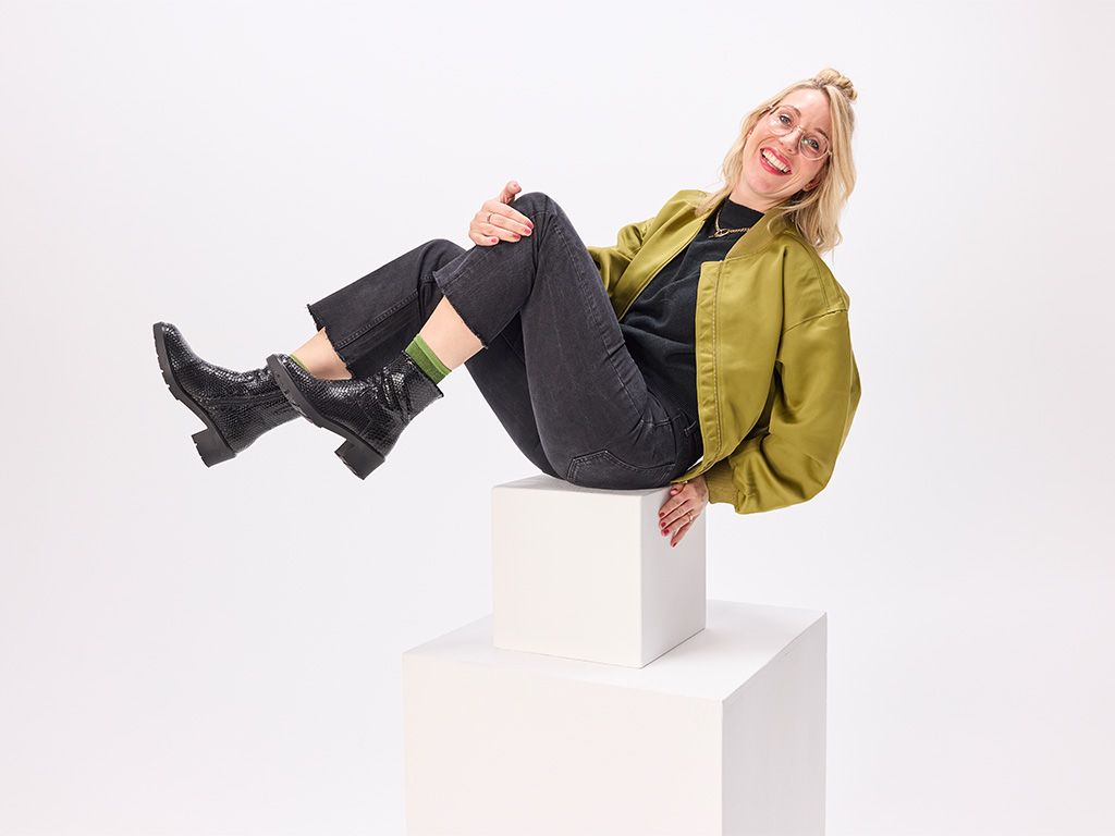 Frau im Studio trägt schwarze Solidus Damen-Stiefeletten mit strukturierter Lederoptik und sitzt lächelnd auf Podesten