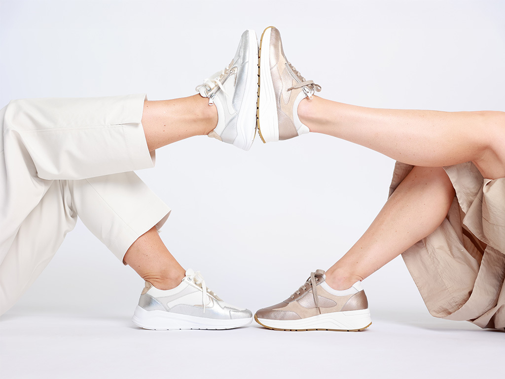 Zwei Frauenbeine bilden einen Kreis, beide tragen Solidus Damen-Sneaker in Weiß/Silber und Beige/Gold vor weißem Hintergrund