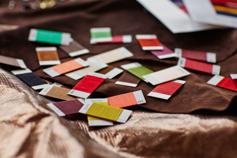 Farbkarten und Materialmuster in Rot, Grün, Orange und Beige auf braunem Leder – Solidus Trend- und Designauswahl