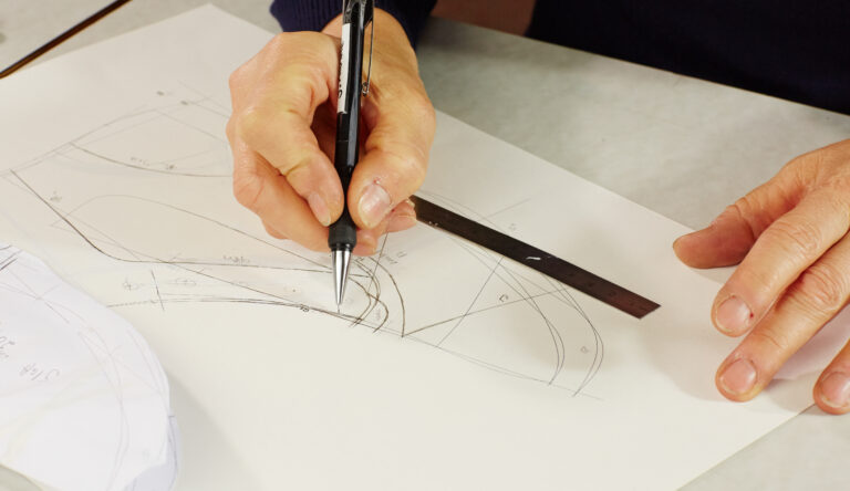 Hände zeichnen mit Stift und Lineal eine Schuh-Designskizze auf Papier – Solidus Entwicklung und Handwerk