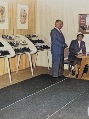 Historisches Farbfoto: Solidus Messestand mit Schuhregalen und drei Personen am Tisch
