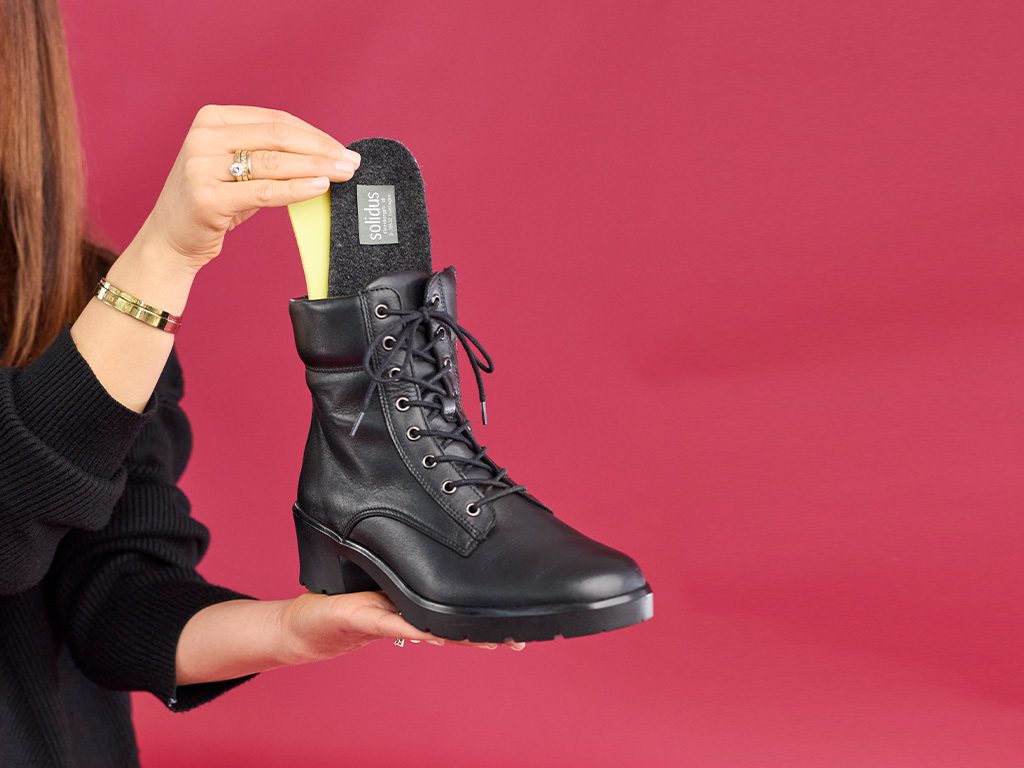 Hand zeigt herausnehmbare Solidus Einlegesohle in einem schwarzen Damen-Schnürstiefel – komfortable Passform und einfacher Wechsel