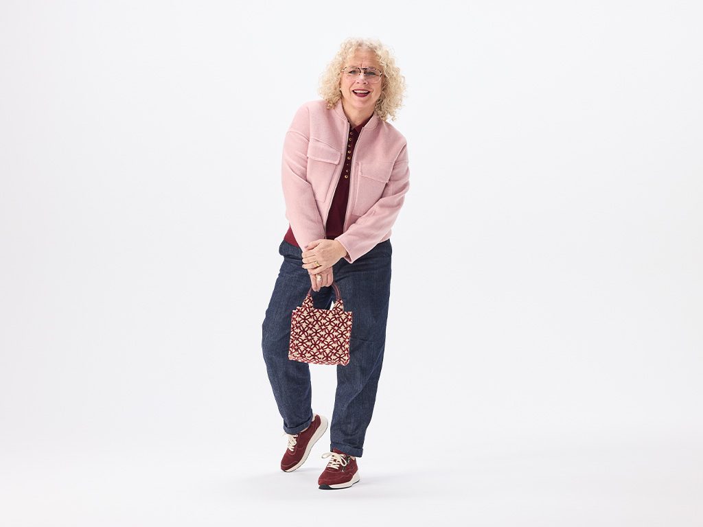 Frau im Studio trägt bordeauxrote Solidus Damen-Sneaker und lächelt, Outfit mit rosa Jacke und Jeans